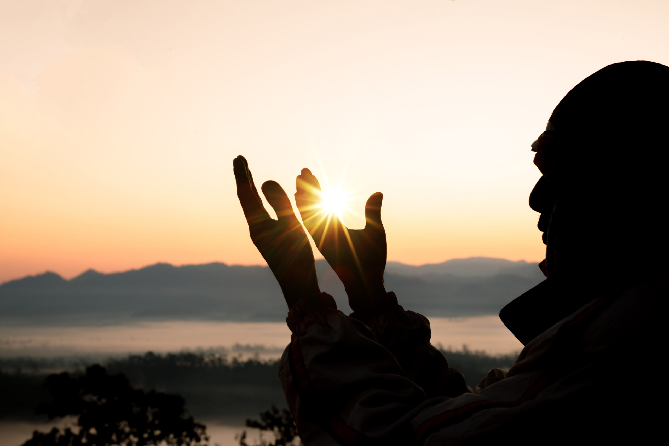 Silhouette of a man raising his hands to make du'a.